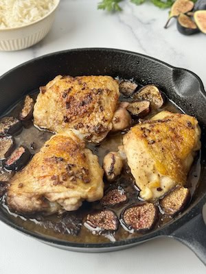 Chicken with figs in a cast iron pan next to parsley and rice.