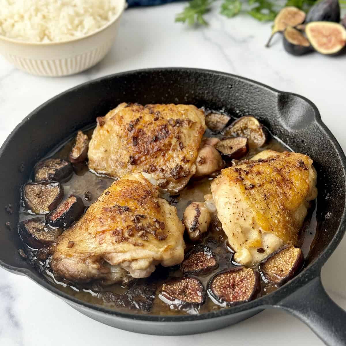 Chicken with figs in a cast iron pan next to parsley and rice.