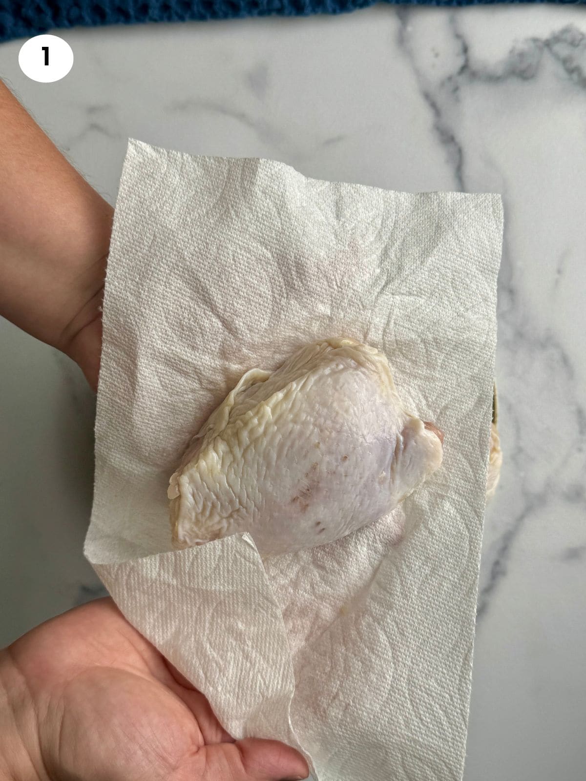 Pat-drying the chicken thighs with a paper towel.