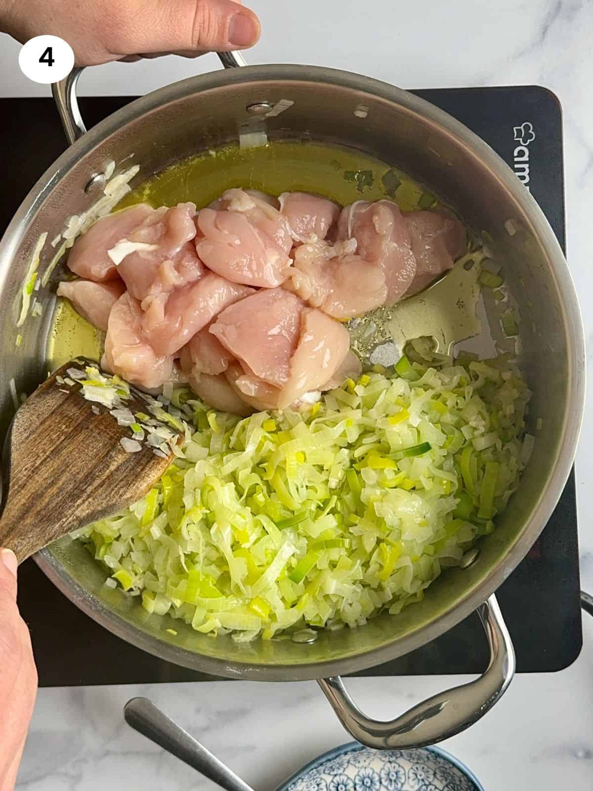 Chicken pieces added to the pot next to the leeks.