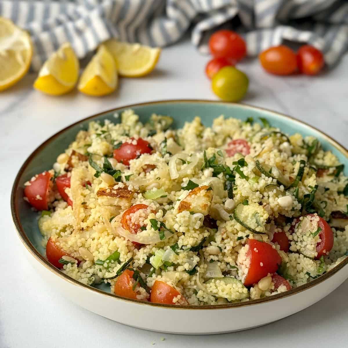 Halloumi and couscous salad served on a plate next to lemon slices and cherry tomatoes.