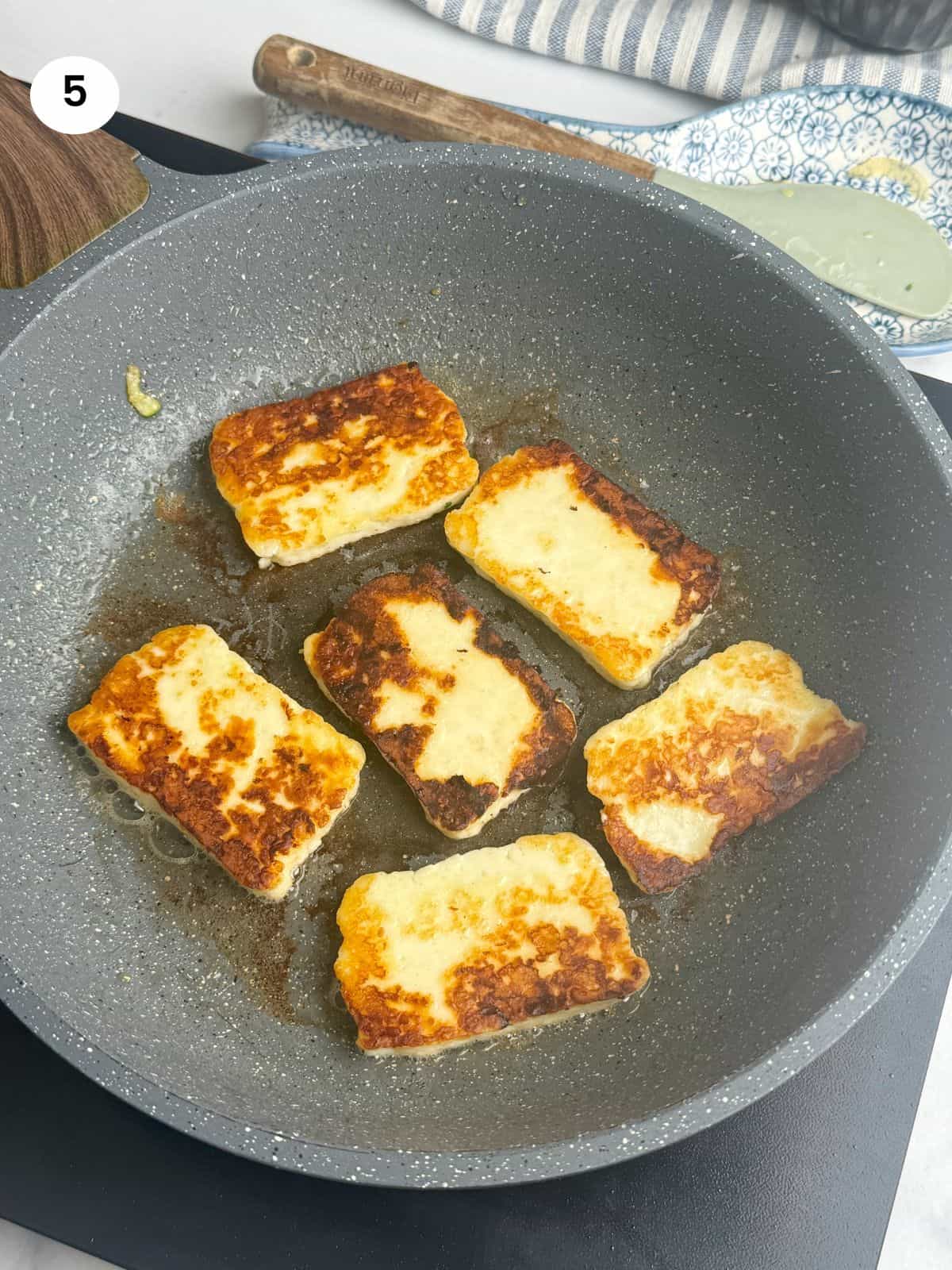 Searing the halloumi slices in a frying pan.