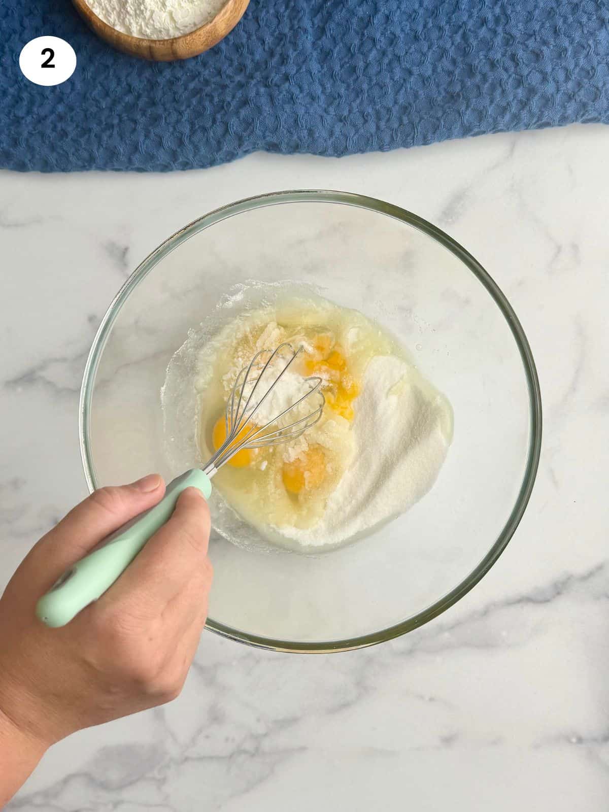 Mixing eggs and sugar in a bowl with a whisk.