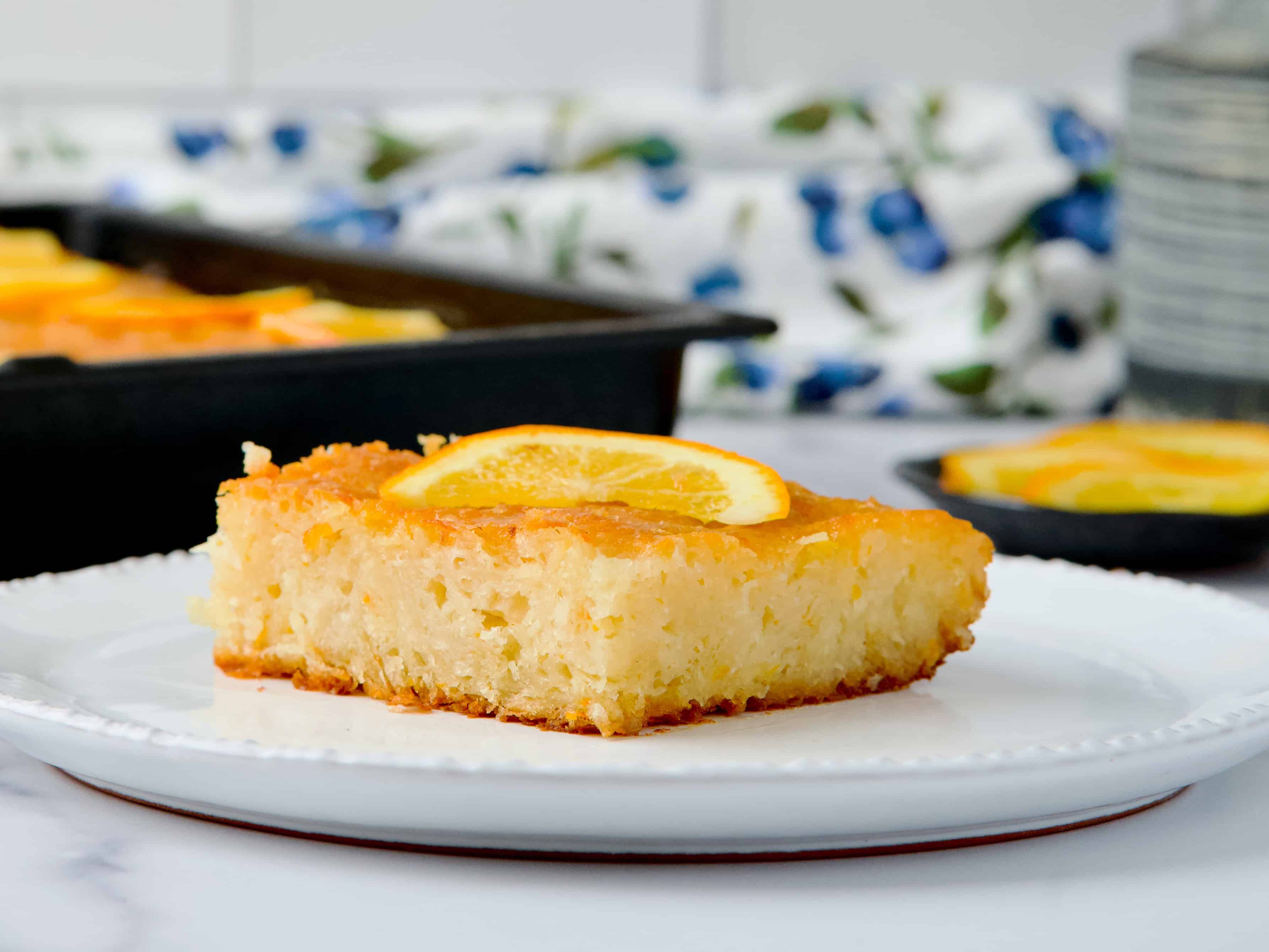 Orange cake slice served on white plate with a slice of orange on top.