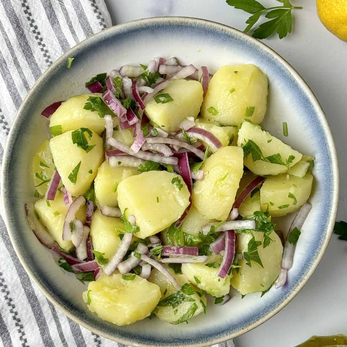 Potato salad served in a bowl next to olive oil bottle, lemon and fresh parsley.