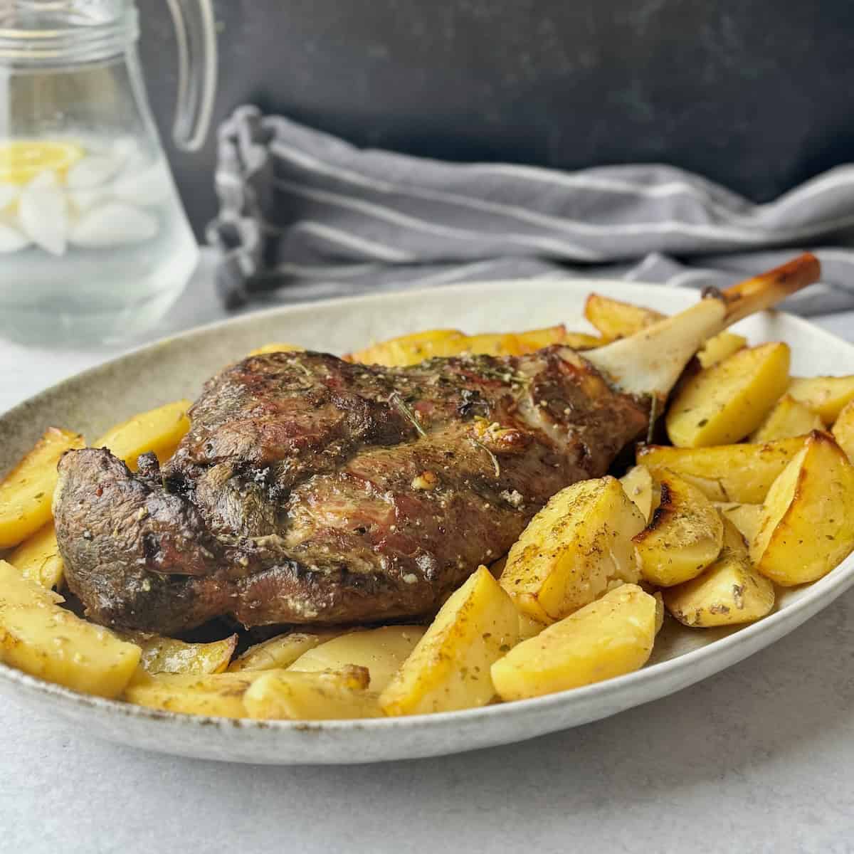 Roasted leg of lamb with potatoes around it in a white serving plate.