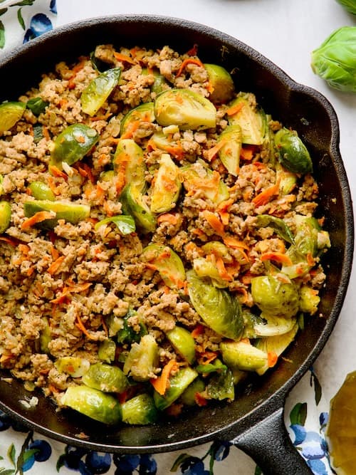 Ground turkey and brussel sprouts in the skillet next to olive oil bottle, sprouts and spices.