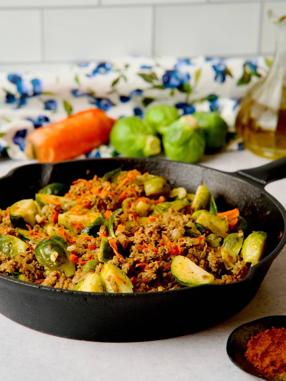 Ground turkey and brussel sprouts in the skillet next to black plate with spices.