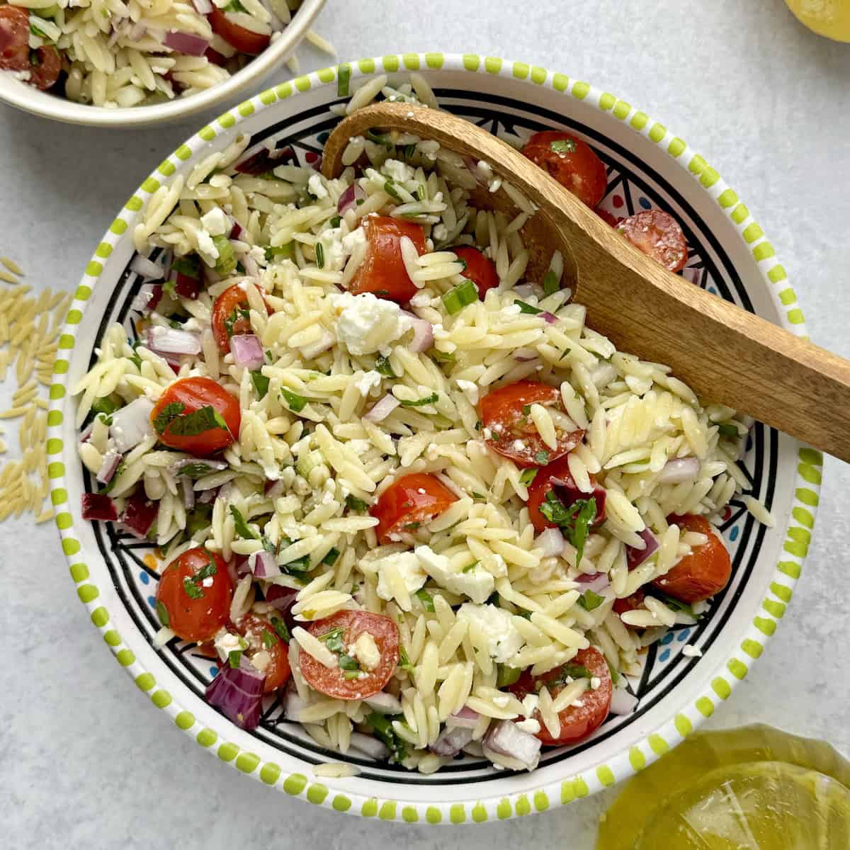 Orzo pasta and feta salad served in bowl next to lemon slices and orzo pasta.