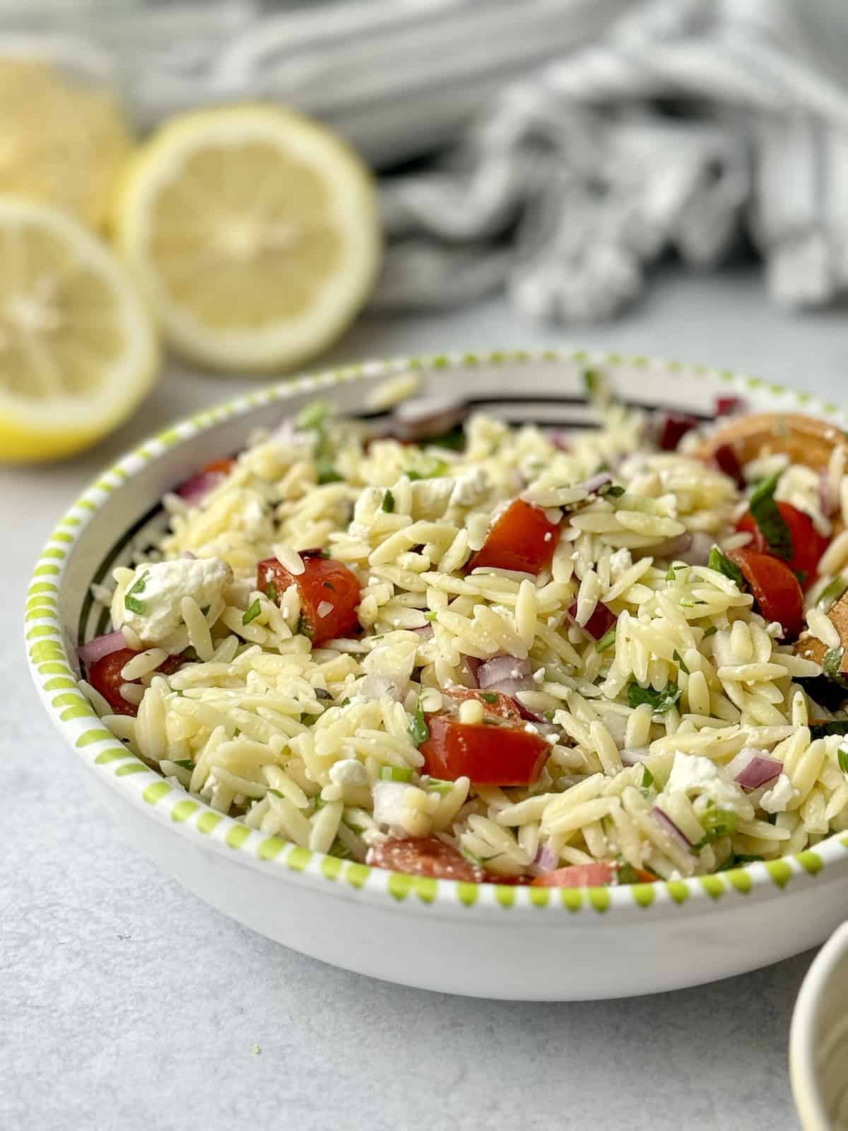 Lemon orzo salad served in white bowl with lemons in the background.