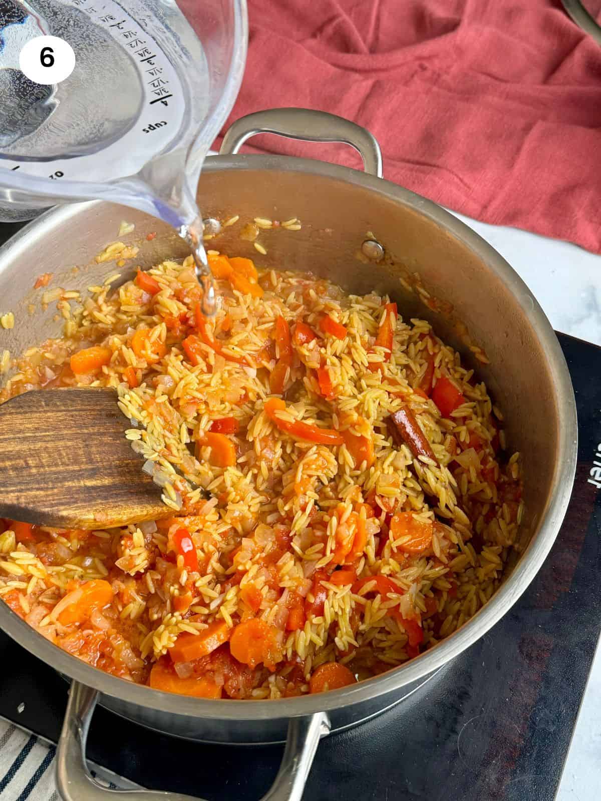 Adding the orzo pasta and water to the pan.