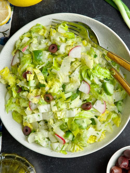 Greek lettuce salad served in a bowl next to halved lemon, fresh dill and olives.