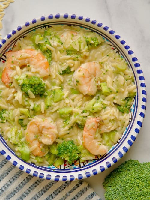 Broccoli and shrimp orzo pasta served in a bowl with broccoli florets and orzo next to the dish.