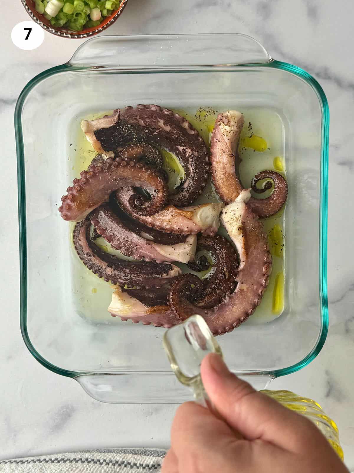 Drizzling olive oil over seared octopus in bowl.