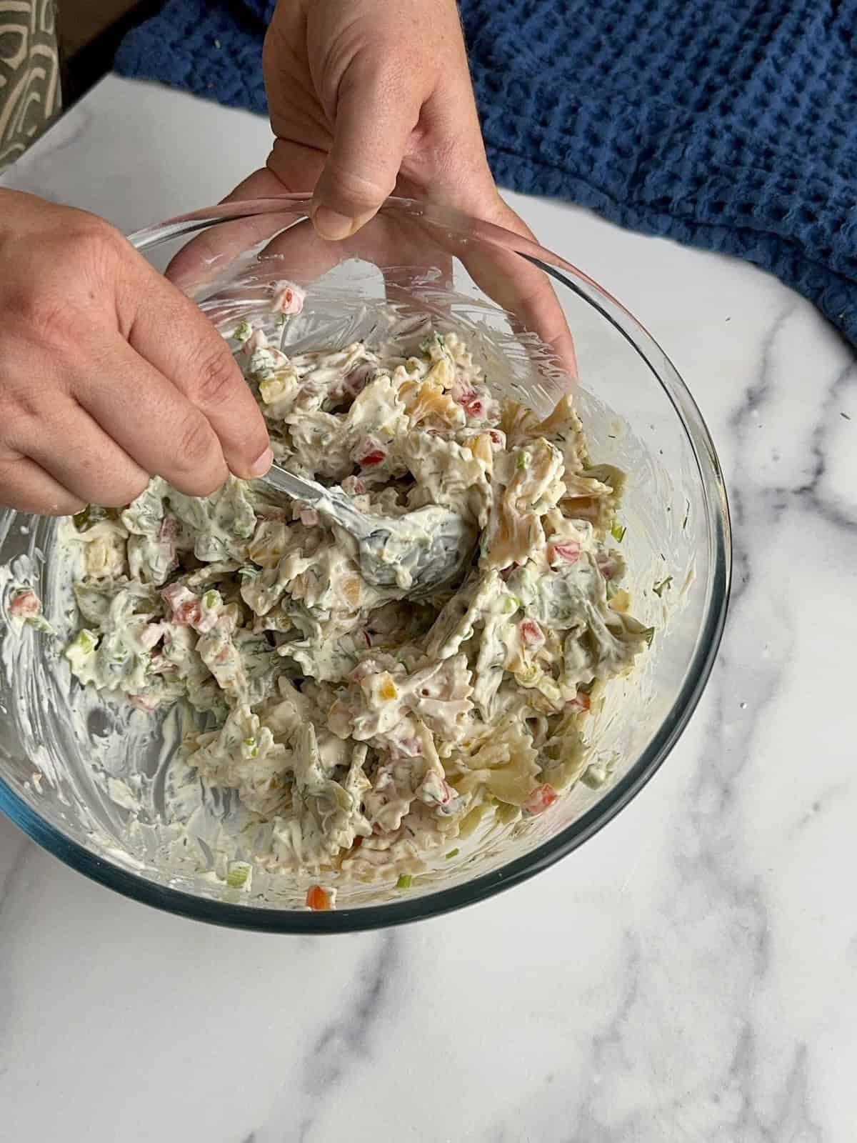 Mixing the pasta and veggies with the Greek yogurt dressing.