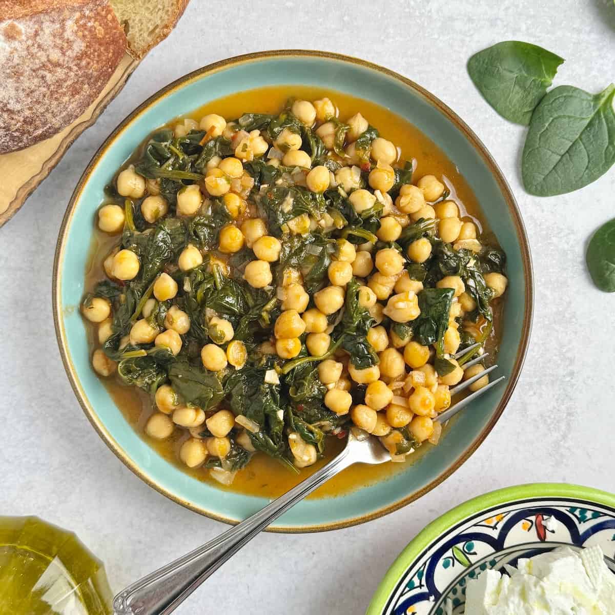Spinach and chickpea stew served in a bowl with slices of bread and olive oil in the background.