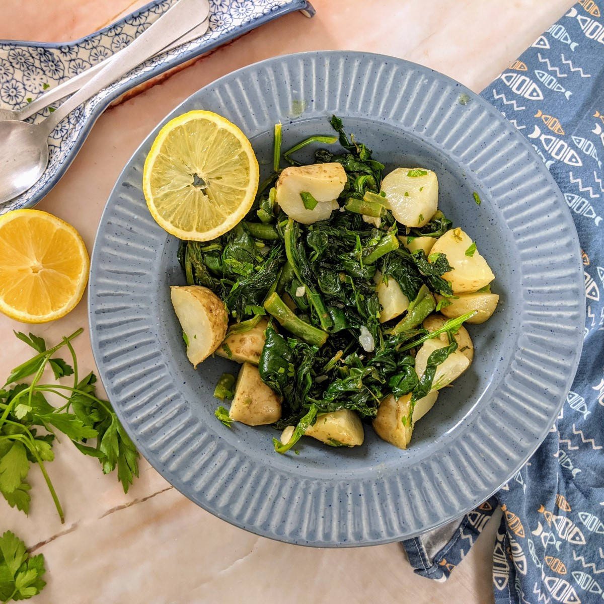 Swiss chard and potatoes salad served with a slice of lemon next to a bunch of parsley and a whole lemon.