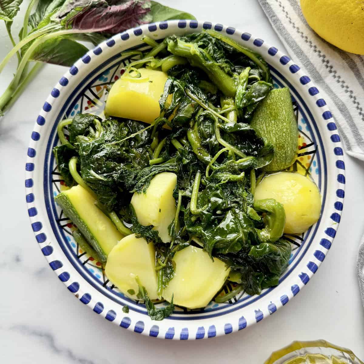 Greek boiled vlita served on a plate next to lemon and raw amaranth greens.