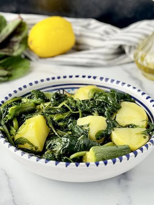 Greek boiled vlita served on a plate next to lemon and raw amaranth greens.